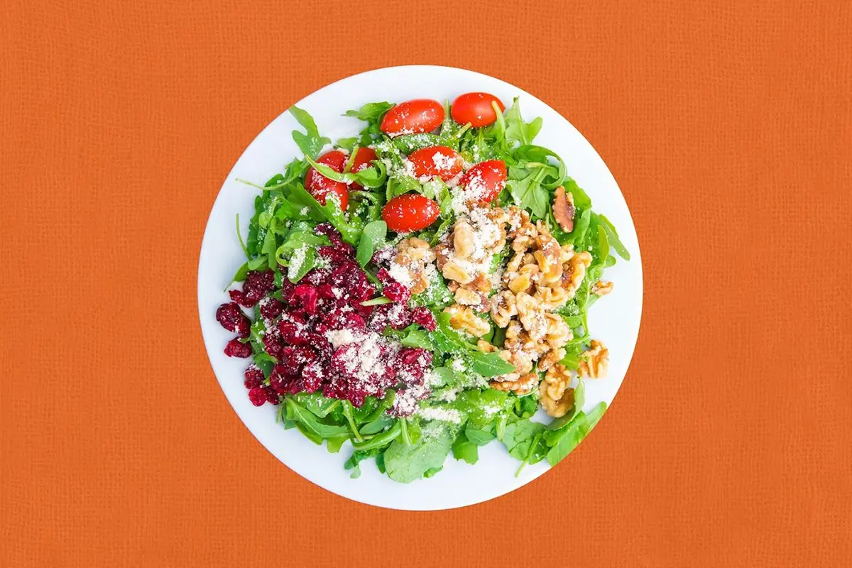 A plate of salad with tomatoes, walnuts and cranberry.