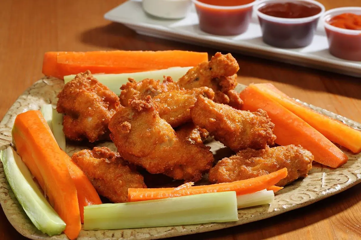 A plate of chicken wings and carrots on the table.